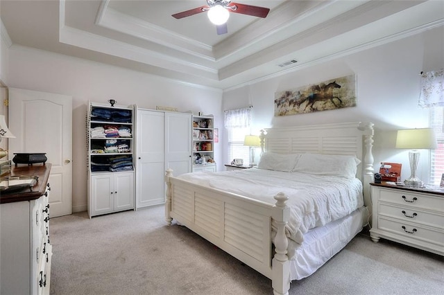 carpeted bedroom with ceiling fan, a tray ceiling, and ornamental molding