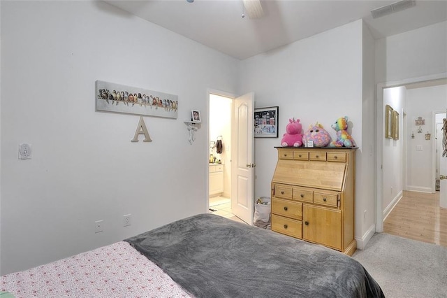 bedroom with ceiling fan, light colored carpet, and ensuite bath