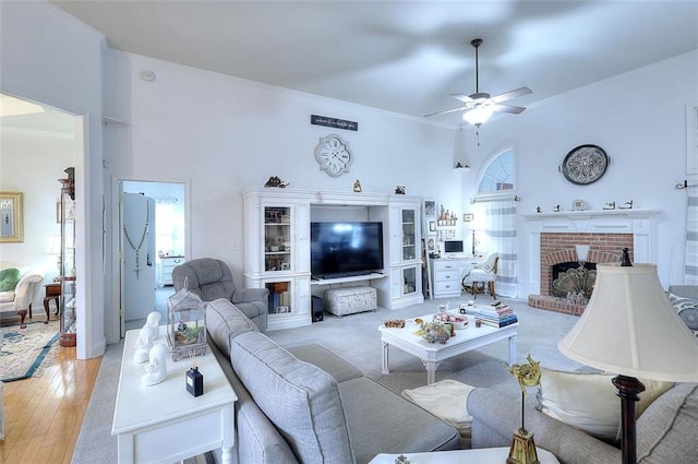 living room with a brick fireplace, crown molding, light hardwood / wood-style flooring, and ceiling fan