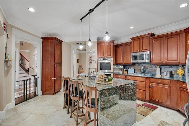 kitchen featuring a kitchen island with sink, hanging light fixtures, dark stone countertops, appliances with stainless steel finishes, and a kitchen bar