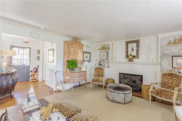 living area with light wood-style flooring, a brick fireplace, and ornamental molding