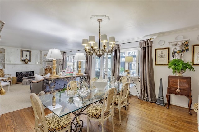 dining room featuring baseboards, a fireplace, light wood-style floors, crown molding, and a notable chandelier