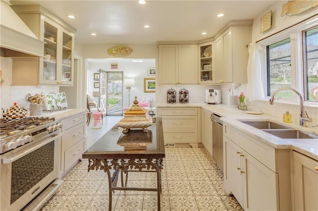 kitchen with custom range hood, cream cabinetry, stainless steel range with gas stovetop, and a sink