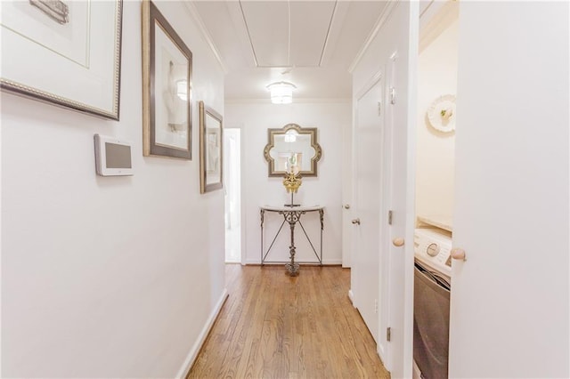 corridor with baseboards, attic access, light wood-style flooring, washer / clothes dryer, and crown molding