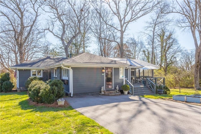 ranch-style home with a deck, a front yard, driveway, and a shingled roof