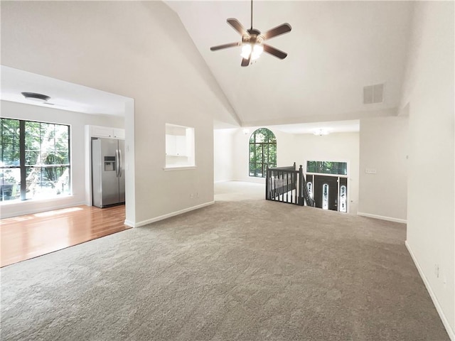 unfurnished living room with ceiling fan with notable chandelier, high vaulted ceiling, and carpet flooring