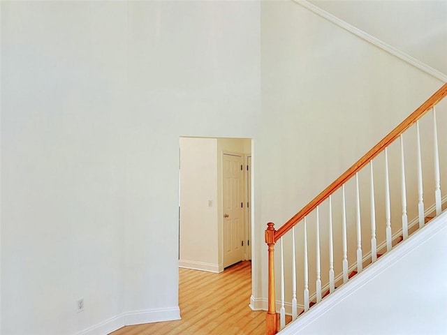 stairway featuring a high ceiling, baseboards, and wood finished floors