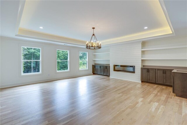 unfurnished living room with a large fireplace, light hardwood / wood-style floors, a raised ceiling, and a notable chandelier