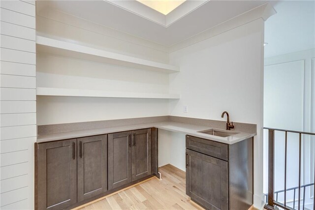 bar with dark brown cabinets, light wood-type flooring, and sink