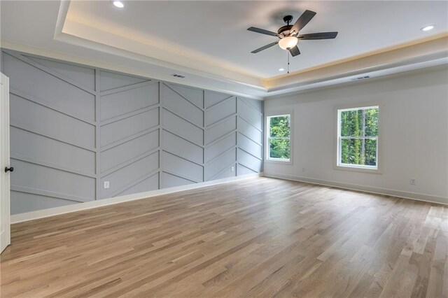 empty room featuring ceiling fan, a tray ceiling, and light hardwood / wood-style flooring