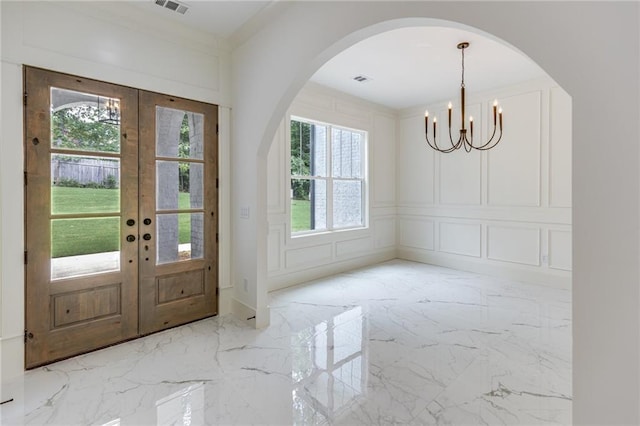 foyer with an inviting chandelier, crown molding, and french doors