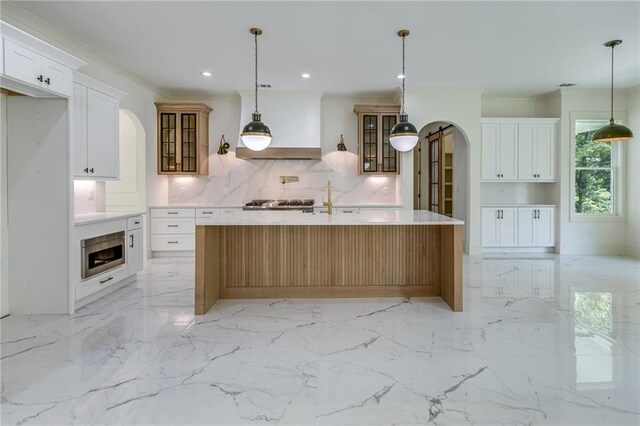 kitchen featuring tasteful backsplash, a center island with sink, white cabinets, and hanging light fixtures