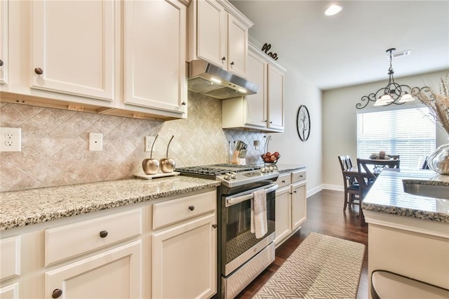 kitchen featuring dark wood-style floors, gas stove, baseboards, under cabinet range hood, and tasteful backsplash