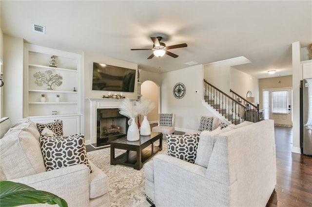 living room featuring a ceiling fan, visible vents, dark wood finished floors, a fireplace, and stairs