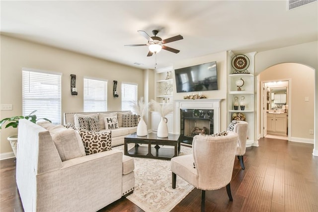 living room featuring visible vents, dark wood-style floors, a high end fireplace, arched walkways, and ceiling fan