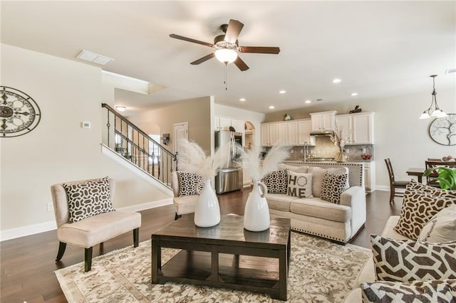 living area with stairway, dark wood-style floors, baseboards, visible vents, and ceiling fan