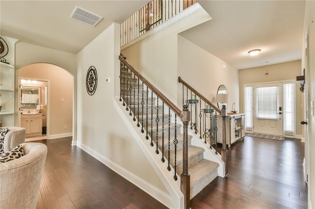 foyer entrance with dark wood-style floors, visible vents, baseboards, arched walkways, and stairs