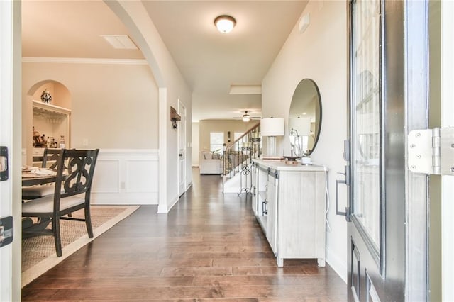 foyer entrance with a wainscoted wall, ornamental molding, a ceiling fan, a decorative wall, and dark wood-style flooring