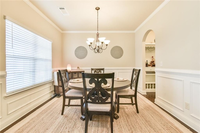 dining space featuring arched walkways, a notable chandelier, crown molding, and a decorative wall