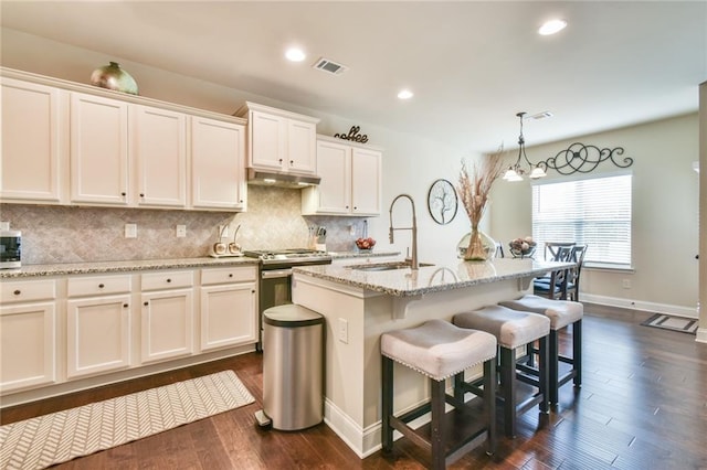 kitchen with visible vents, stainless steel gas range, a sink, under cabinet range hood, and tasteful backsplash