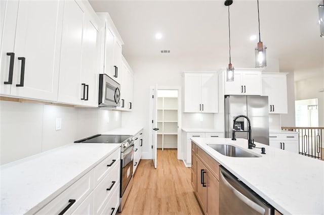 kitchen with a sink, white cabinets, appliances with stainless steel finishes, light wood finished floors, and decorative light fixtures