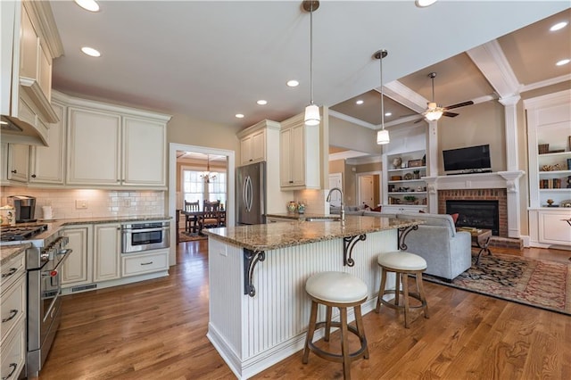 kitchen featuring ceiling fan, a sink, stainless steel appliances, open floor plan, and stone counters