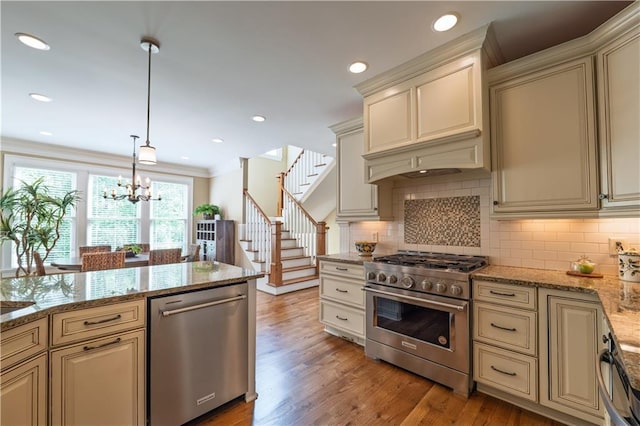 kitchen with appliances with stainless steel finishes, cream cabinets, light stone countertops, and backsplash