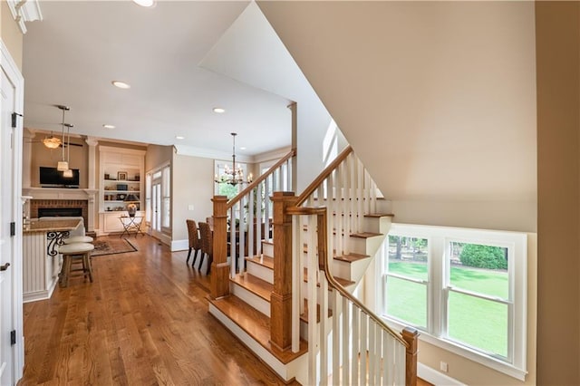 stairway with a notable chandelier, a fireplace, recessed lighting, baseboards, and wood finished floors