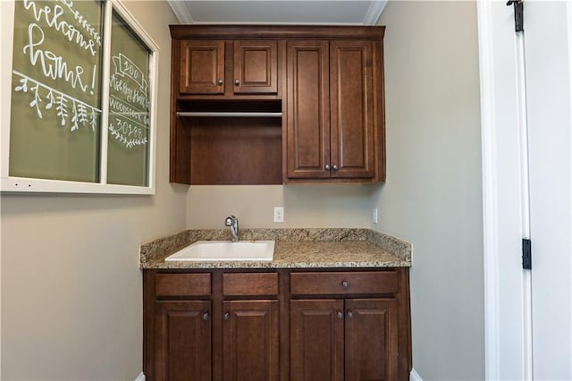 bar featuring crown molding, baseboards, and a sink