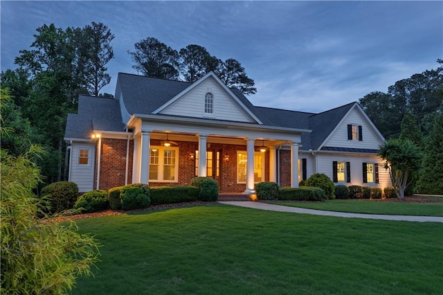 neoclassical / greek revival house featuring brick siding, a shingled roof, covered porch, and a front yard