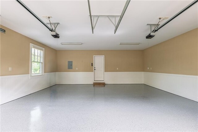 garage featuring a garage door opener, wainscoting, and electric panel