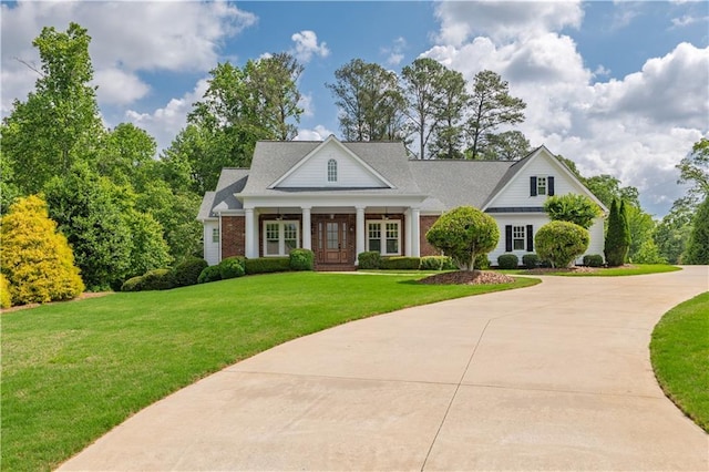 neoclassical / greek revival house with curved driveway, a front lawn, covered porch, and brick siding