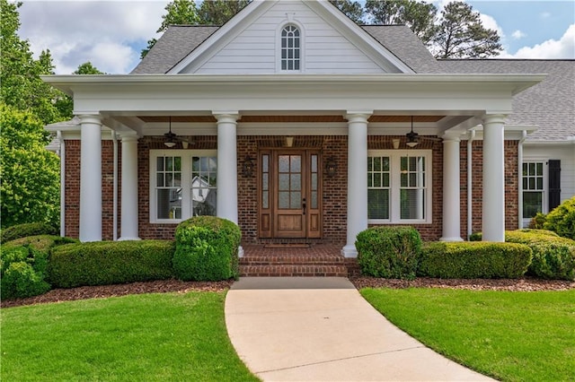 view of exterior entry with a lawn, brick siding, and a ceiling fan