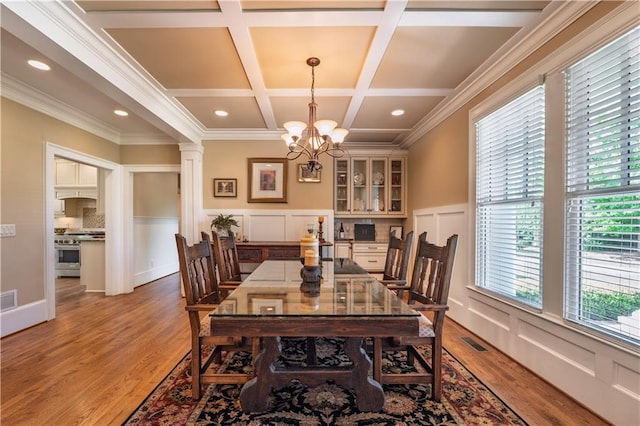 dining area with visible vents, crown molding, a notable chandelier, a decorative wall, and light wood-style flooring
