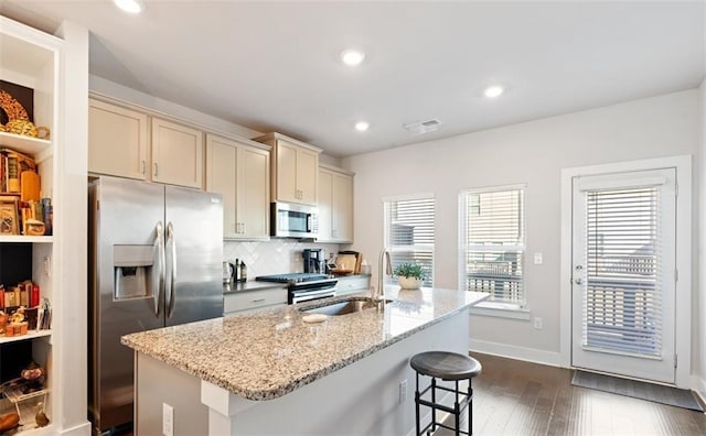 kitchen with sink, cream cabinets, an island with sink, a breakfast bar area, and appliances with stainless steel finishes