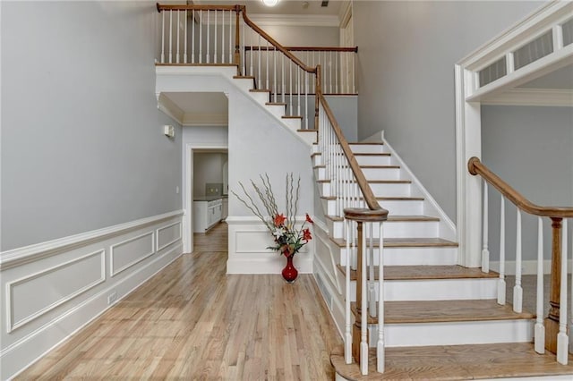 stairway with a decorative wall, wainscoting, crown molding, and wood finished floors