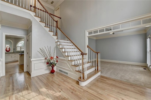 stairway featuring visible vents, wood finished floors, a high ceiling, crown molding, and a decorative wall