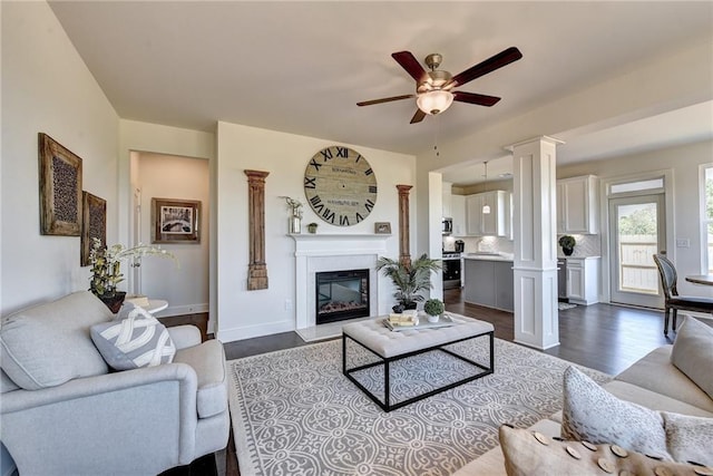 living room with dark wood-type flooring, ceiling fan, and decorative columns