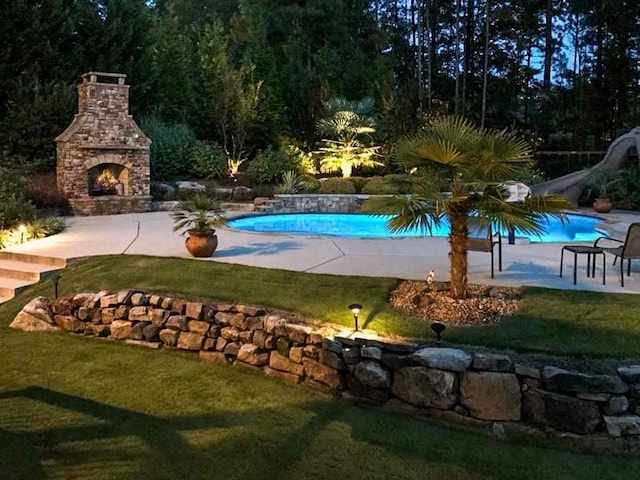 view of pool with a yard, a patio, an outdoor stone fireplace, and a water slide