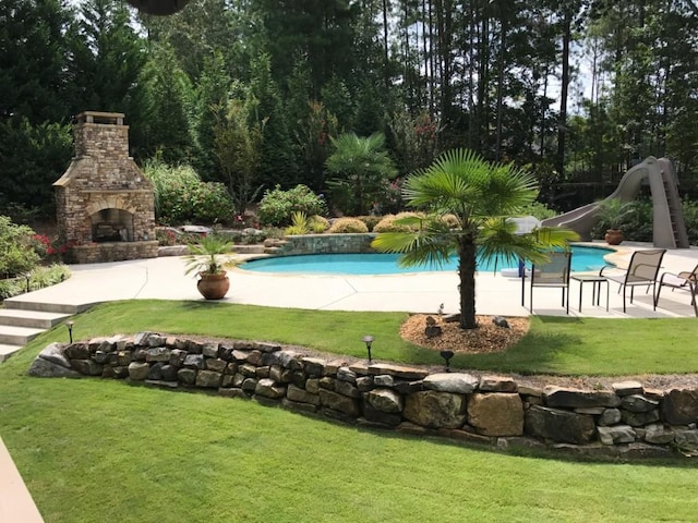 view of pool featuring a water slide, a yard, an outdoor stone fireplace, and a patio area