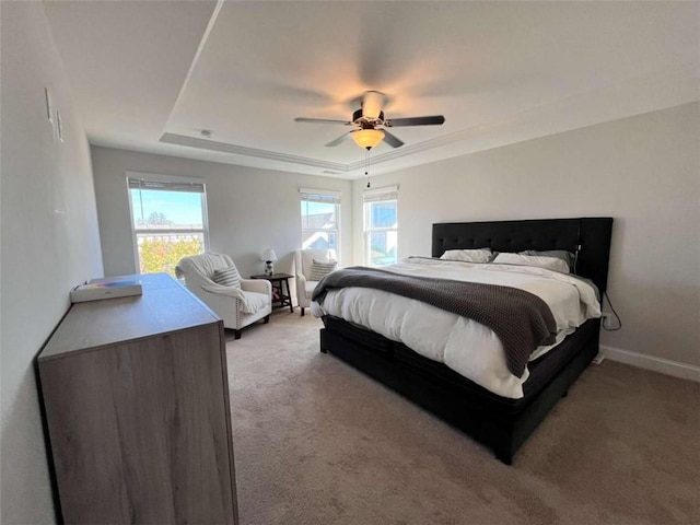 carpeted bedroom with ceiling fan and a tray ceiling