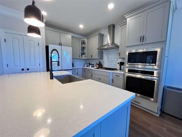 kitchen with sink, hanging light fixtures, stainless steel appliances, decorative backsplash, and wall chimney range hood