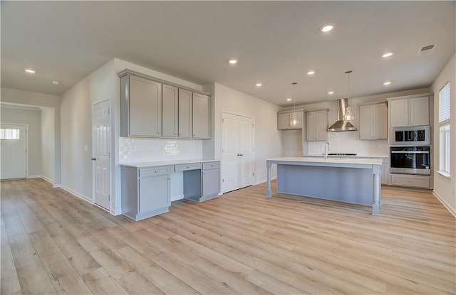 kitchen featuring built in microwave, wall chimney exhaust hood, gray cabinetry, pendant lighting, and oven