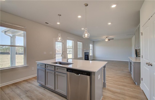 kitchen with sink, gray cabinetry, decorative light fixtures, dishwasher, and a kitchen island with sink