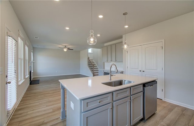 kitchen with gray cabinets, dishwasher, sink, hanging light fixtures, and a center island with sink