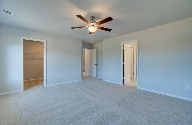 unfurnished bedroom featuring a walk in closet, light carpet, ceiling fan, and a closet