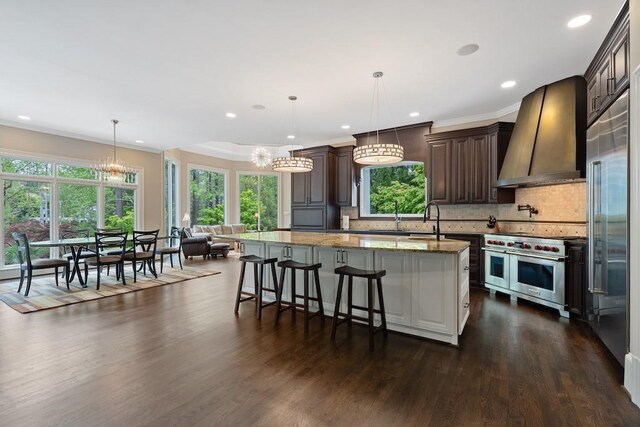 kitchen with high quality appliances, premium range hood, decorative backsplash, light stone countertops, and a kitchen island