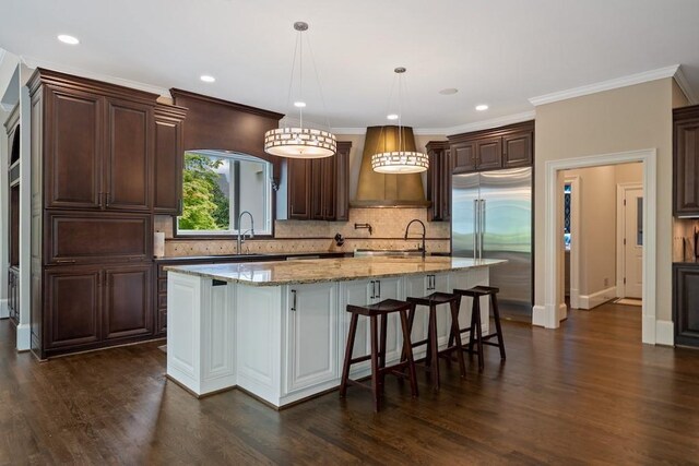 kitchen featuring built in fridge, sink, dark hardwood / wood-style floors, an island with sink, and decorative light fixtures