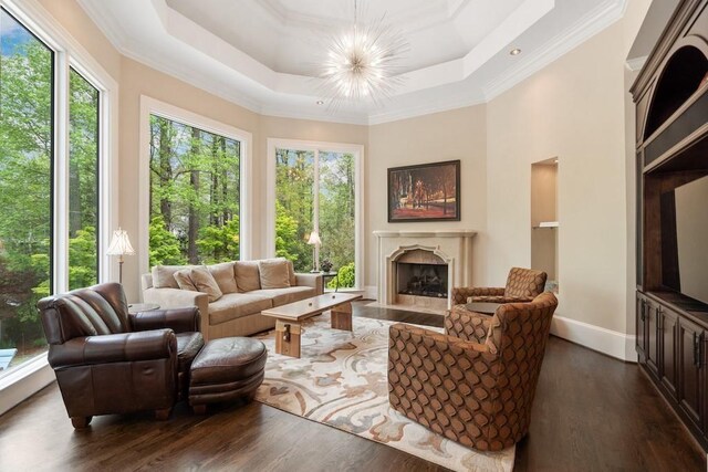 living room featuring dark hardwood / wood-style flooring, a high end fireplace, a notable chandelier, crown molding, and a tray ceiling