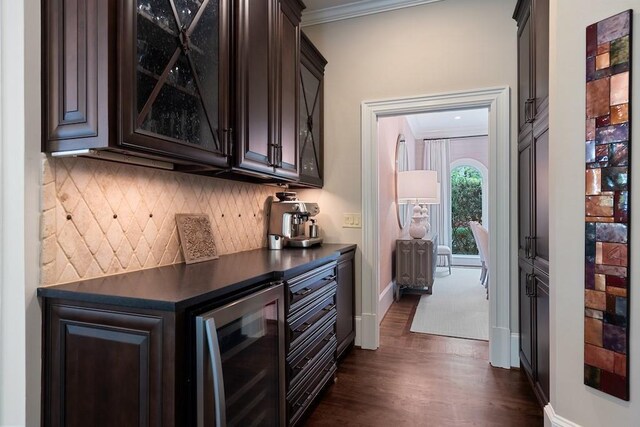 bar with dark hardwood / wood-style floors, ornamental molding, tasteful backsplash, dark brown cabinetry, and beverage cooler